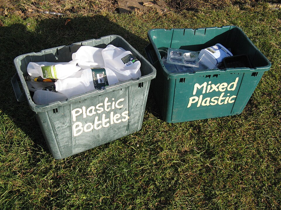 잔디 위에 놓인 초록색 수거함 두 개에 각각 ‘Plastic Bottles(플라스틱 병)’과 ‘Mixed Plastic(혼합 플라스틱)’이라 적혀 있고 플라스틱 용기가 담겨 있다